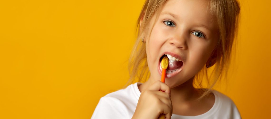 Charming Little Girl In White T Shirt Cleaning Teeth With Colorful Kids Toothbrush Looking At Camera
